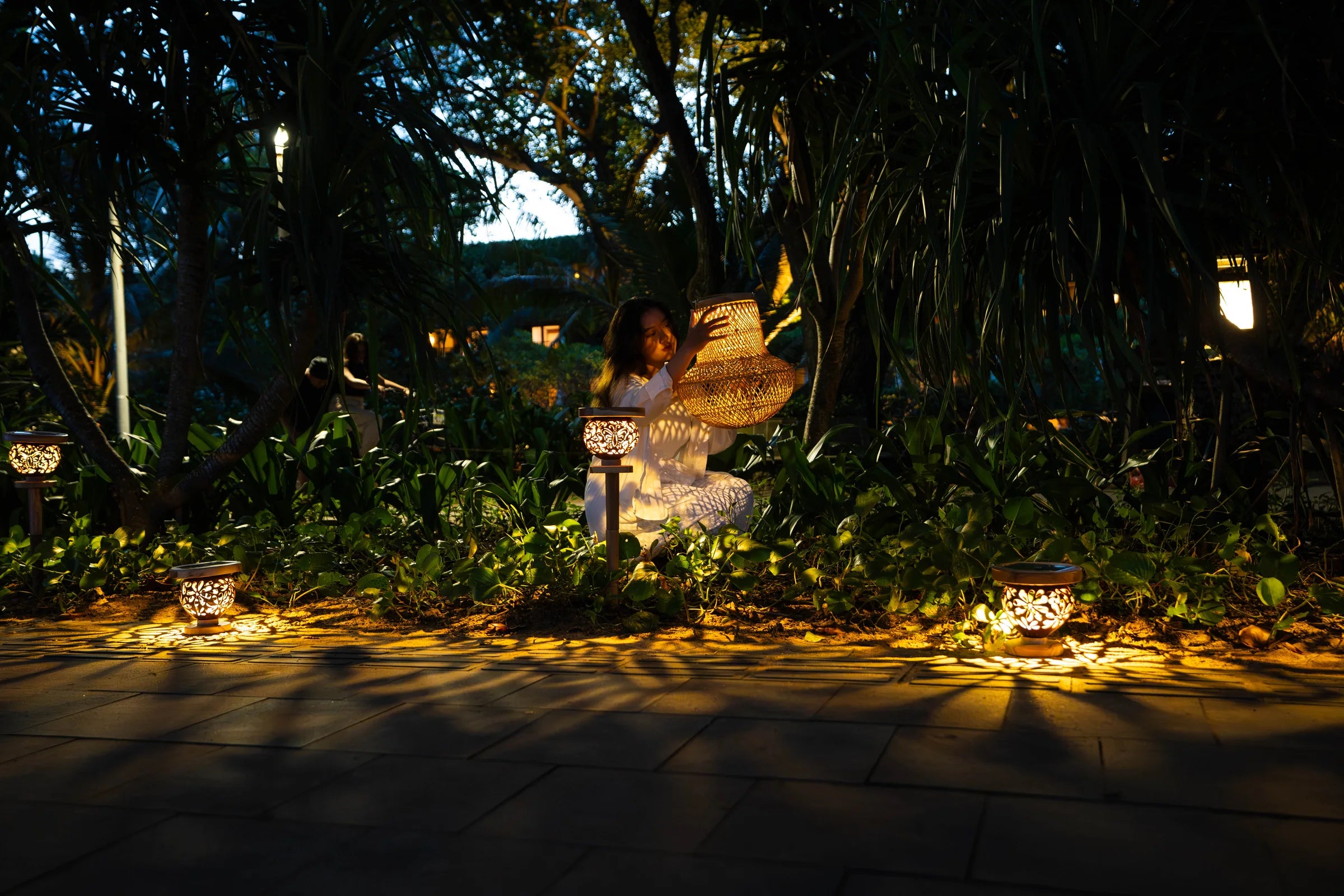 Woman holding a glowing rattan solar lantern in a garden